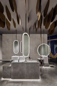 Modern restroom interior with marble countertops, concrete sinks, and illuminated mirrors.