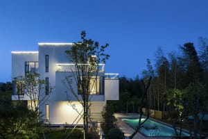 A modern residential building with a white exterior and concrete walls, illuminated at night with warm lights.