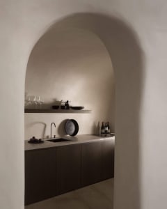 A minimalist kitchen with a concrete countertop, dark cabinets, and modern fixtures.