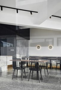 Industrial-style restaurant interior with concrete and terrazzo flooring, black chairs, and minimalist design.