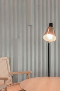 A minimalist interior space featuring wood and concrete materials with a floor lamp and round wooden table.