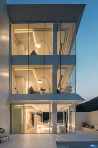 A modern glass house with a minimalist design, illuminated at night, showcasing cozy lighting and a serene atmosphere.