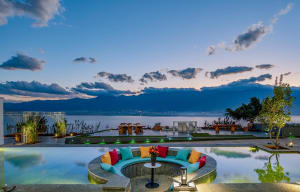 A circular seating area with colorful cushions overlooking a serene lake and mountains at dusk.