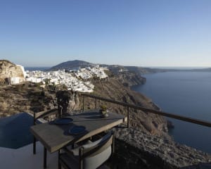 A wooden table and chairs overlooking the ocean and a coastal town on a cliffside.