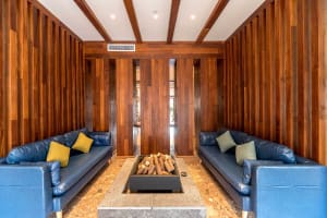 A modern interior living room with wooden walls and blue sofas arranged around a fire pit.