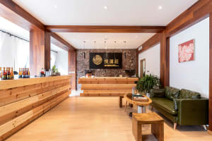 Modern lobby interior with wooden furniture and decor, featuring a green leather sofa, wooden tables, and a reception desk.