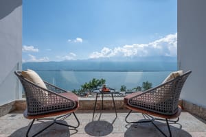 Two modern patio chairs with cushions and a small table with tea set, overlooking a vast ocean under a clear blue sky with sc