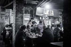 A bustling street food restaurant adorned with rustic brick and concrete walls, featuring patrons dining at tables.