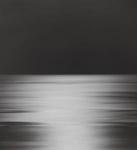 A black and white photograph of a blurred ocean scene at night