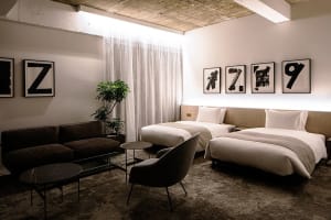 A modern hotel room with two twin beds, a brown sofa, and framed numbers on the wall.