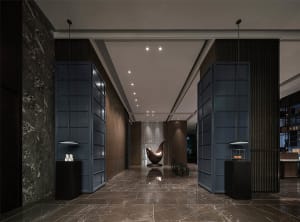 A modern minimalist lobby with a sleek metal chair, marble floor, and glass elements.