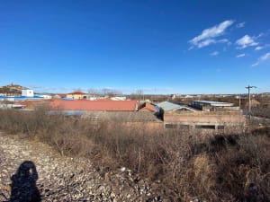 A view of a rural town with buildings made of concrete and brick, under a clear blue sky with scattered clouds.