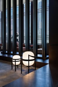 A modern hotel lobby with glass columns and light fixtures, featuring decorative vases on a wooden floor.
