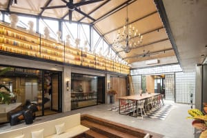 Large industrial style office with glass walls, concrete accents, and exposed beams. Features a shared workspace with a long 