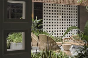 Outdoor seating area with wicker chairs, wooden stools, and greenery