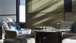 Modern living room with a comfortable fabric chair and metal coffee table, featuring light and shadow play from an unseen sou