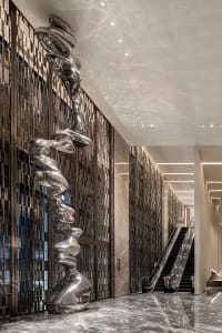 A modern lobby featuring a metal sculpture as a centerpiece, with a sleek, gray floor and tall walls.