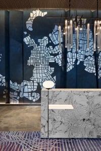 A modern lobby featuring a marble wall with a map pattern, ambient lighting, and geometric hanging lights.