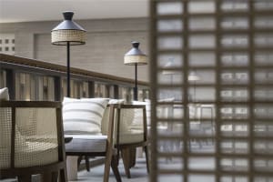 Modern restaurant bar with wooden cane seating and textile cushions, featuring sleek floor lamps with woven shades.