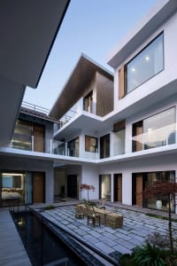 Modern residential exterior with glass walls, wooden accents, and concrete flooring.