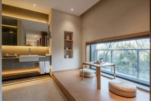 Modern minimalist bathroom with concrete walls and floor, large window, and sitting area with tea table and stools.