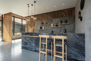 A minimalist coffee shop counter made of dark marble with wooden stools and decorative vases on the wall.