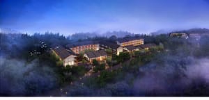 Aerial view of a hotel resort with illuminated rooms and pathways surrounded by trees at dusk.