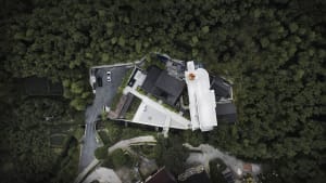 Aerial view of a modern residential house surrounded by dense greenery, featuring a white rooftop.