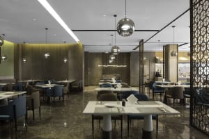 Modern restaurant interior with white marble tables and chairs, pendant lights, and green accents.