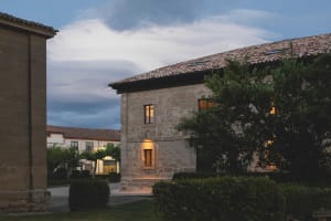 Stone building with clay tile roof illuminated at dusk with clouds in the sky
