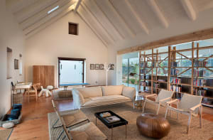 A minimalist modern living room with wood and fabric materials, featuring a light-colored sofa and chairs, a wooden floor, an