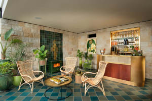A modern living room with green and blue tiled floor, rattan chairs, and a bar area with bottles and glasses.