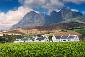 A picturesque village with white tiled rooftops surrounded by lush green fields and dramatic mountains in the background.