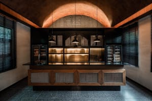 A sleek, modern kitchen with metallic finishes and industrial lighting features a bar area with a high ceiling and arched lig