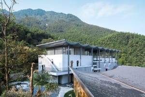 A modern residential building with concrete, glass, and wood exterior materials, surrounded by nature.