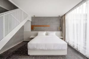 Modern bedroom with white bed, minimalist design, and textured grey wall behind the headboard.