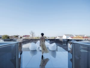A modern rooftop space featuring glass furniture and a single individual.