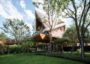 Modern exterior of a treehouse with wood and metal accents, glass windows, and a slide.