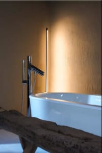 A simplistic bathroom featuring a sleek ceramic bathtub and a modern, minimalist sink faucet in a well-lit room.