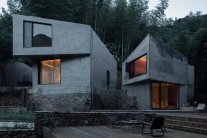 A modern residential home with a minimalist concrete exterior features large windows and a deck.