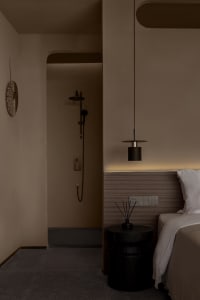 A modern bedroom featuring dark wood flooring, matte black metal accents, and textured beige walls.