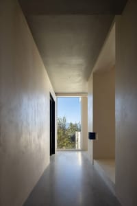 A minimalist hallway with concrete walls and a view of the outdoors through a large window.