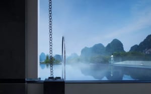 A modern resort features a glass swimming pool with a scenic view of mountains and mist.