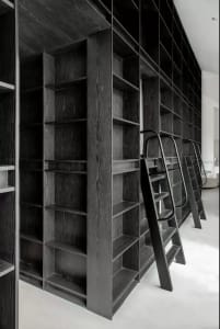 A spacious, minimalist dark wood library with built-in shelves and metal ladders.