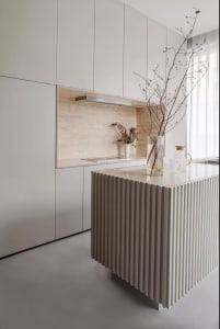 Minimalist kitchen with white walls, a white ribbed kitchen island, and a marble backsplash.