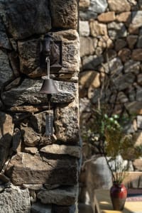 A rustic metal bell mounted on a stone wall.