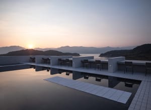 A minimalist landscape featuring concrete structures and a calm body of water at sunset.