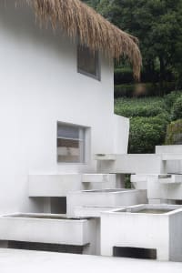 A modern building with a concrete exterior features a thatched roof and geometric planters.