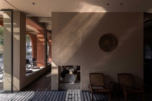 A modern lobby featuring concrete walls and floor tiles with geometric patterns, illuminated by natural light.