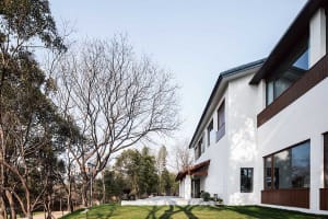 A modern residential home with a white exterior and concrete patio surrounded by trees.